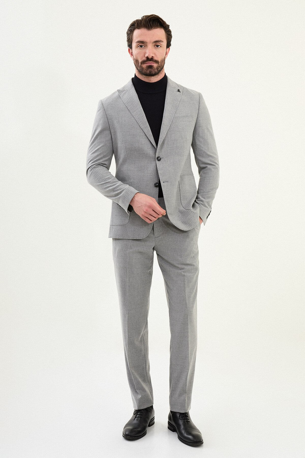 Men’s gray slim-fit mono-collar (mandarin collar) performance suit with 2-button single-breasted jacket, minimalist patch pockets, matte micro-texture fabric, styled with a black turtleneck.