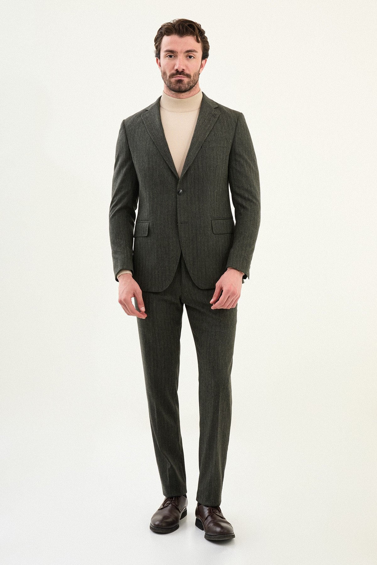 Men’s olive-toned khaki herringbone slim-fit single-breasted suit with structured shoulders and tailored waist, high-wool blend fabric with stretch for winter wear, styled with a cream fine-gauge turtleneck.
