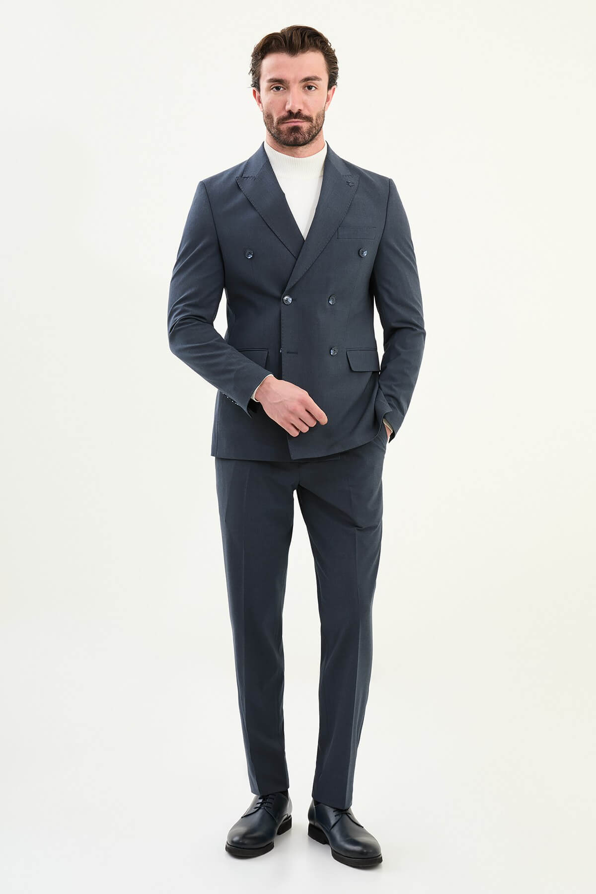 Men’s navy blue slim-fit double-breasted 6x2 suit with peak lapels, matte micro-texture finish, cotton-wool-viscose blend with stretch for wrinkle-resistant wear, styled with a white turtleneck.